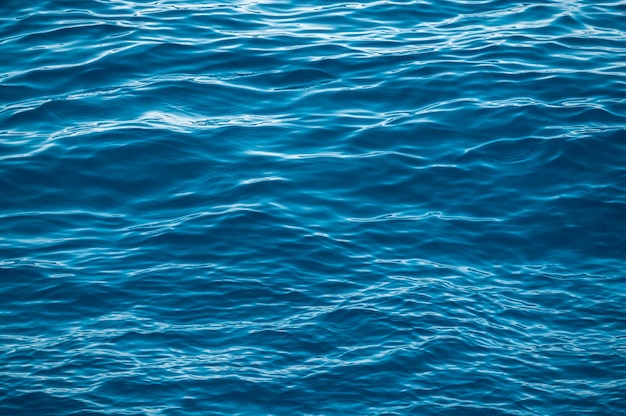 blue water surface with bright sun light reflections water in ocean or sea background closeup