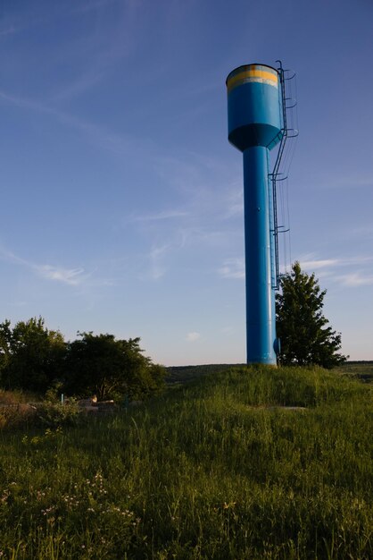 A blue water tower against a blue sky in the middle of a green lawn to supply the settlement with cl