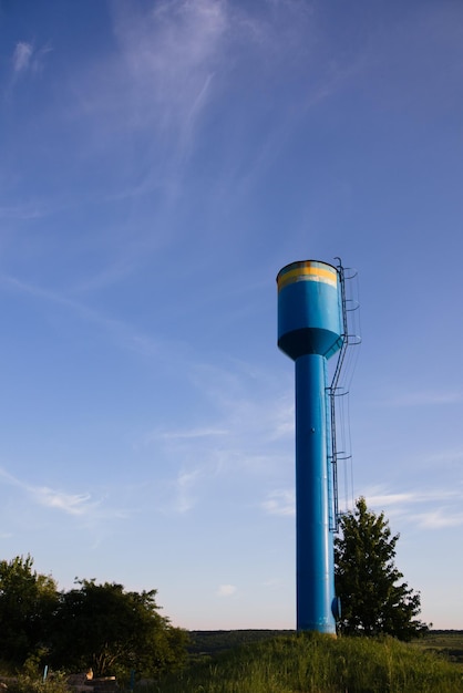 A blue water tower against a blue sky in the middle of a green lawn to supply the settlement with cl