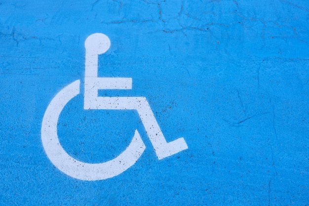 Blue and white handicapped sign painted on the floor of a parking lot