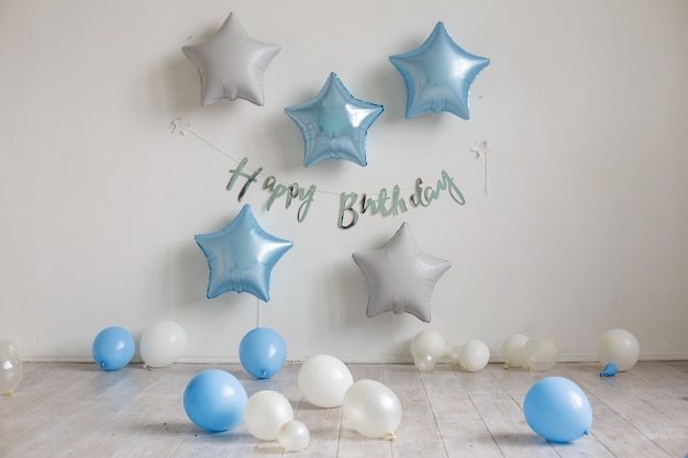 Blue and white star balloons and the inscription Happy birthday on the white wall. Birthday decor