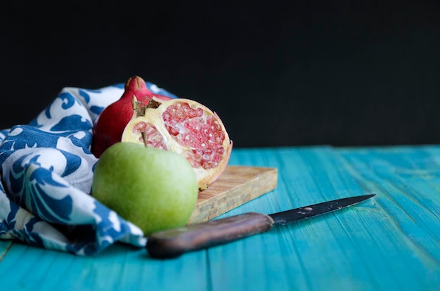 Blue wooden table against black background with pomegranates and green apple over a cut board Selective focus