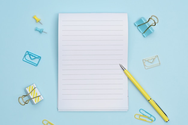 Blue and yellow stationary items and notebook on blue background with copy space. Blank notebook for notes or checklist.