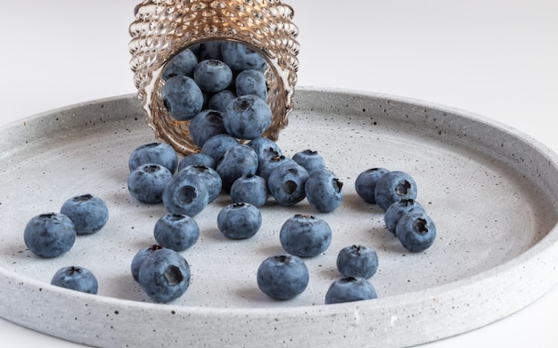 Blueberries in a glass bowl scattered on a gray plate.