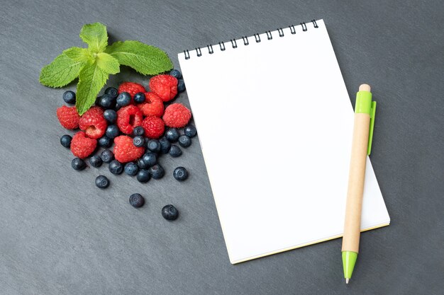 Blueberries, raspberries, mint and notepad for writing notes