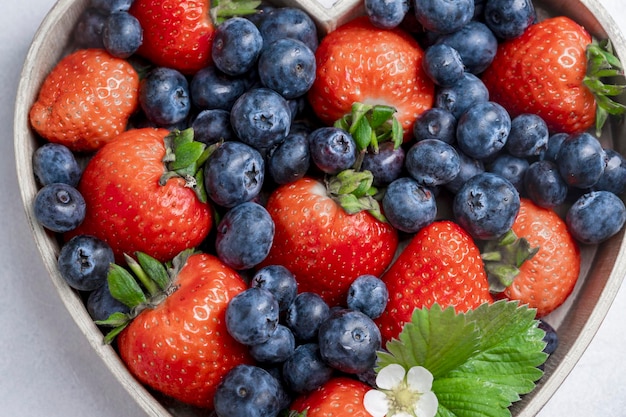 Blueberries and strawberry in wooden heart shape bowl on bright background