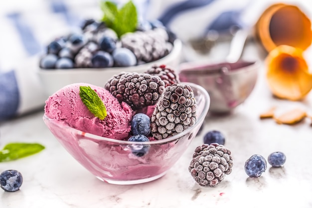 Blueberry and blackberry ice cream in bowl with frozen fruits.