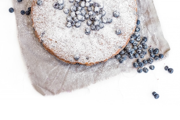 Blueberry cake with fresh bluberries and sugar powder on a beige fabric over a white surface