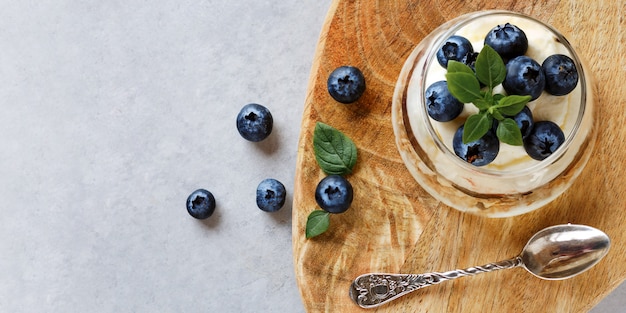 Blueberry dessert with curd cream and granola topping basil leaves on wooden stand. Blueberry jam. Top view.