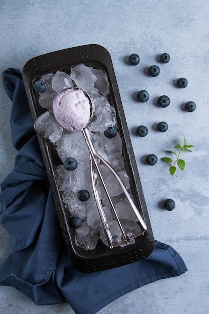 Blueberry ice cream container with a spoon on a gray table fresh blueberries