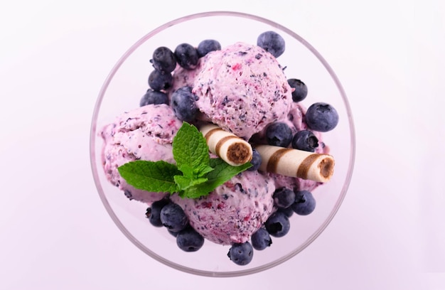 Blueberry ice cream garnished with blueberries and mint on a white plate. Flat lei.