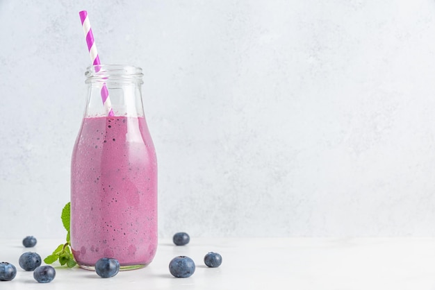 Blueberry smoothie or milkshake in a glass bottle with straw and mint on white background