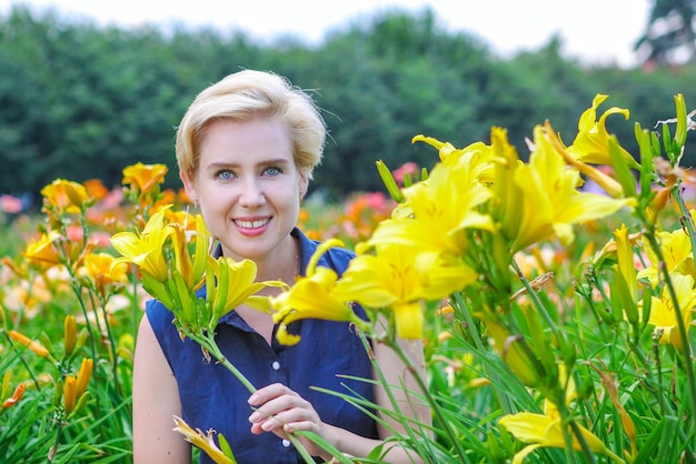 Blueeyed blonde woman among lushly blooming yellow lilies in the garden