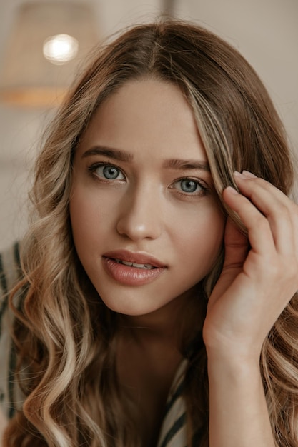 Blueeyed young lady looks into camera Closeup inside portrait of curly blonde attractive woman t