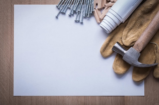 Blueprints sheet of paper steel nails claw hammer wooden dowels and leather protective gloves on wood board copy space construction concept