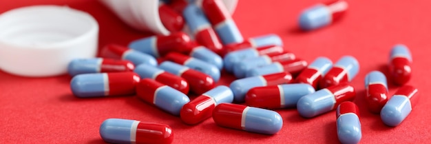 Bluered medical pills scattered from jar lie on a red background uncontrolled drug use concept