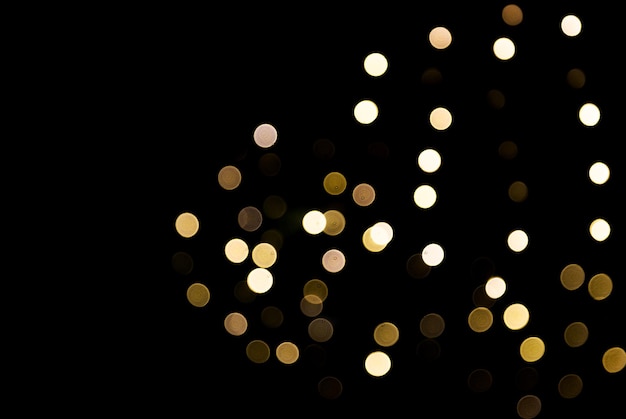 Blurred abstract golden sparkling lights background on black backdrop. Festive concept. Place for design.