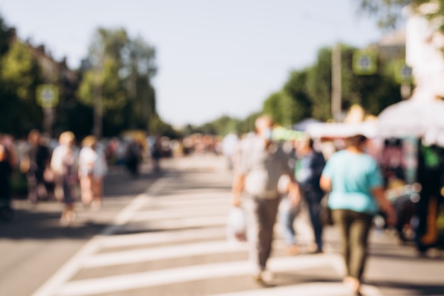 Blurred background, defocus people walk down street on sunny summer day. Concept of holiday, event, crowd of people .