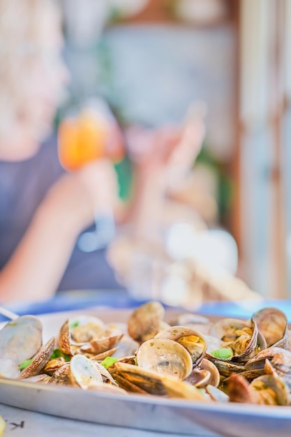 Blurred background with a dish of boiled vongole clams on a table in a cafe vertical frame in the background the silhouette of a woman with a glass of wine Idea for a screensaver or banner