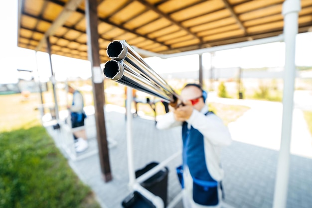 Blurred background with focus on front of shotgun barrel of adult shooter man in sunglasses