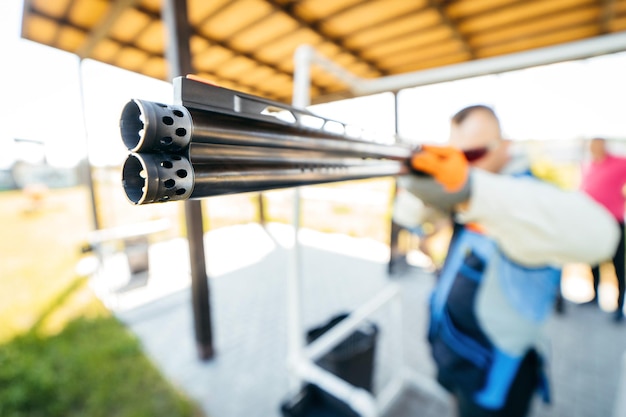 Blurred background with focus on front of shotgun barrel of adult shooter man in sunglasses