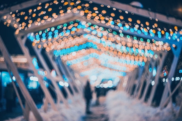 Blurred city with christmas lights at night. New Year bokeh background. Beautiful abstract background with defocused city lights, people. Defocused urban night scene. Design. Concept backdrop. Vintage