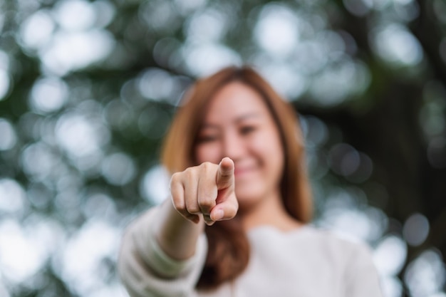 Blurred image of a beautiful young asian woman pointing finger to the camera in the park