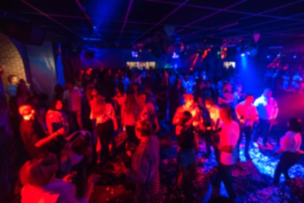 Blurred silhouettes of a group of people dancing in a nightclub on the dance floor under colorful spotlights