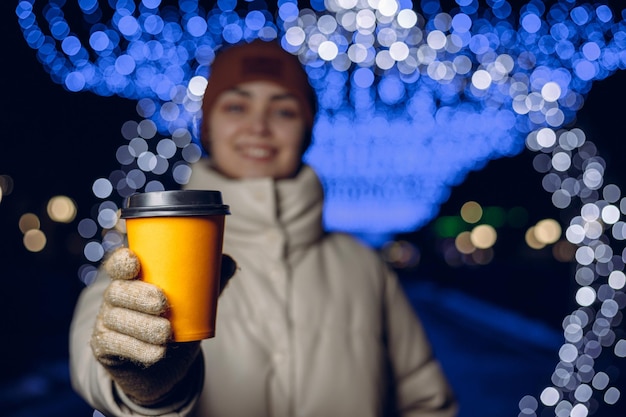 Blurred smiling woman with paper cup of takeaway coffee with mockup copy space in winter city 