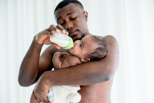 Blurred soft of African father feeding milk from bottle milk to his baby newborn daughter