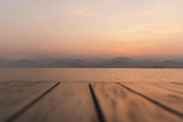 Blurred wooden deck floor with sunrise over river mountain in background