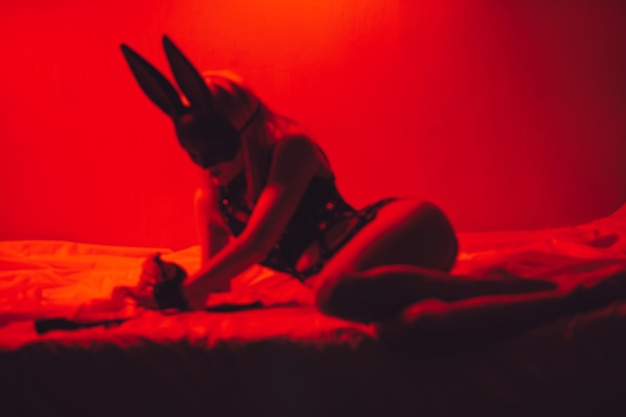 Blurry silhouette of sexy submissive girl in underwear and a mask lies on bed in bedroom BDSM concept of sex