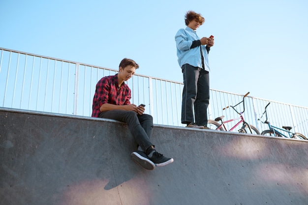 Bmx bikers, teenagers leisures on ramp in skatepark after training. Extreme bicycle sport, dangerous cycle exercise, street riding, biking in summer park