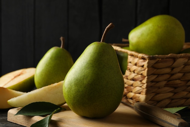 Board and basket with green pears on wooden background