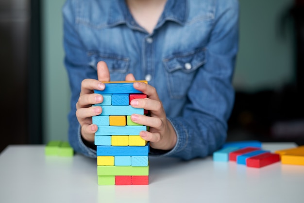 Board game in isolation. Child stay home and playing with multi-colored wooden cubes and building tower.