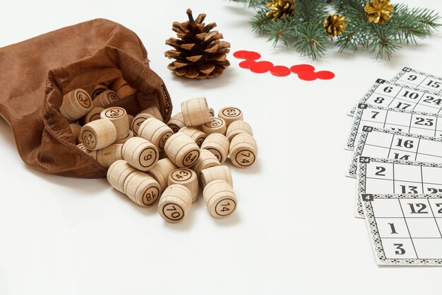 Board game lotto. Wooden lotto barrels with brown bag, game cards and red chips for a game in lotto, Christmas fir tree branches on the background. Shallow depth of field