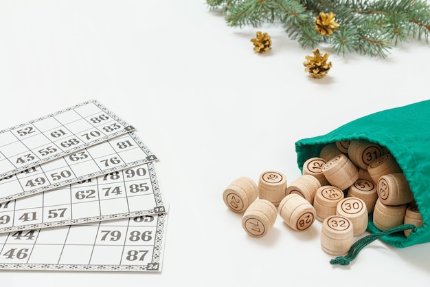 Board game lotto. Wooden lotto barrels with a green bag and game cards. Christmas fir tree branches on the background. Shallow depth of field