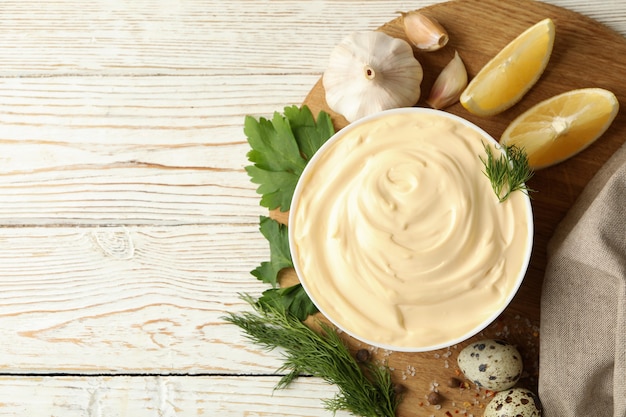 Board with bowl of mayonnaise and ingredients for cooking on wooden background