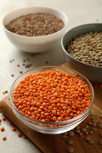 Board with bowls with legumes on white textured table