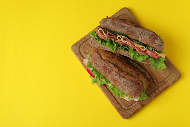 Board with ciabatta sandwiches on yellow background