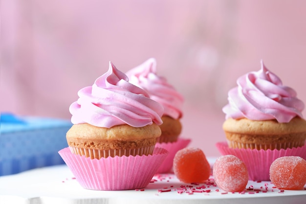 Board with delicious cupcakes and marmalade candies on table