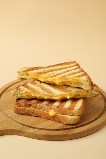 Board with grilled sandwiches on beige background