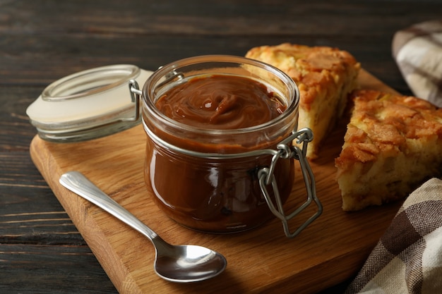 Board with pie and caramel condensed milk on wooden background