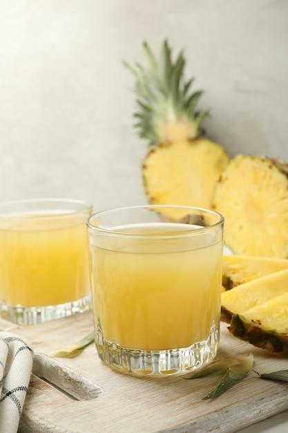 Board with pineapple and glasses with juice