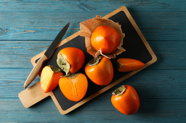 Board with ripe persimmon and knife on wooden background