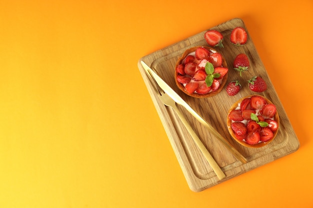 Board with strawberry tarts on orange background.