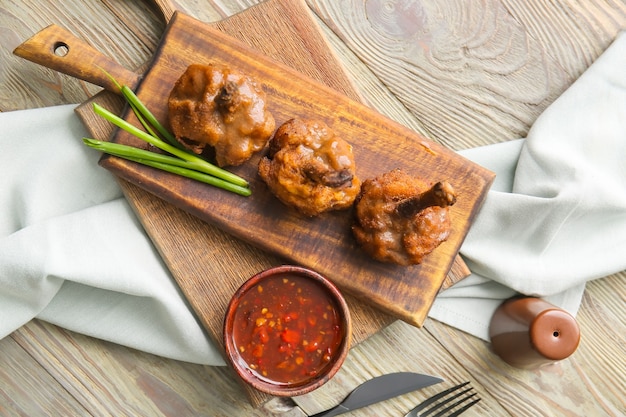 Board with tasty chicken lollipops and sauce on wooden surface