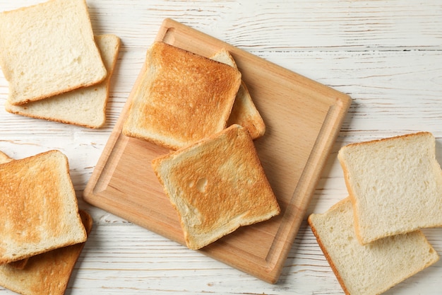 Board with toasts on white wooden background, top view