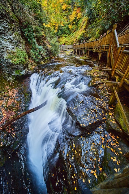 Boardwalk along river with raging falls into abyss and cliffs covered in golden fall leaves