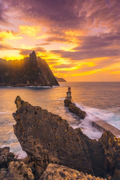 A boat leaving in the orange sunset at the lighthouse of the Pasajes San Juan